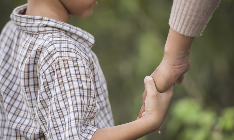 Close up of happy mum and son holding hand in a park. Family concept.