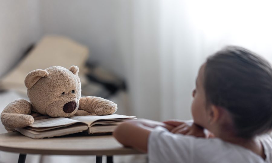 A little girl plays with her teddy bear and a book, teaches him to read, plays at school.